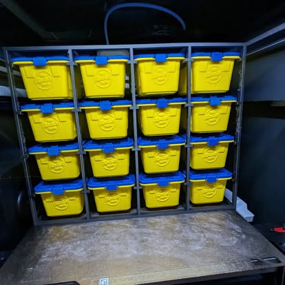 3D printed rack of sixteen mini yellow storage bins with blue lids on the printer bed