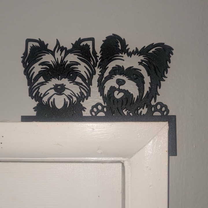 3D printed black silhouettes of two small dogs peeking over a door frame