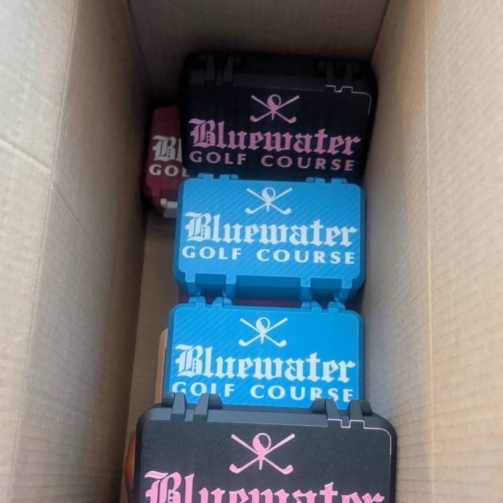 A shipping box full of 3D printed cases printed in several colors for a golf course