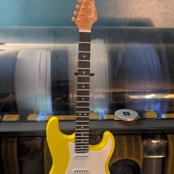 3D printed mini yellow and white electric guitar in front of filament spools