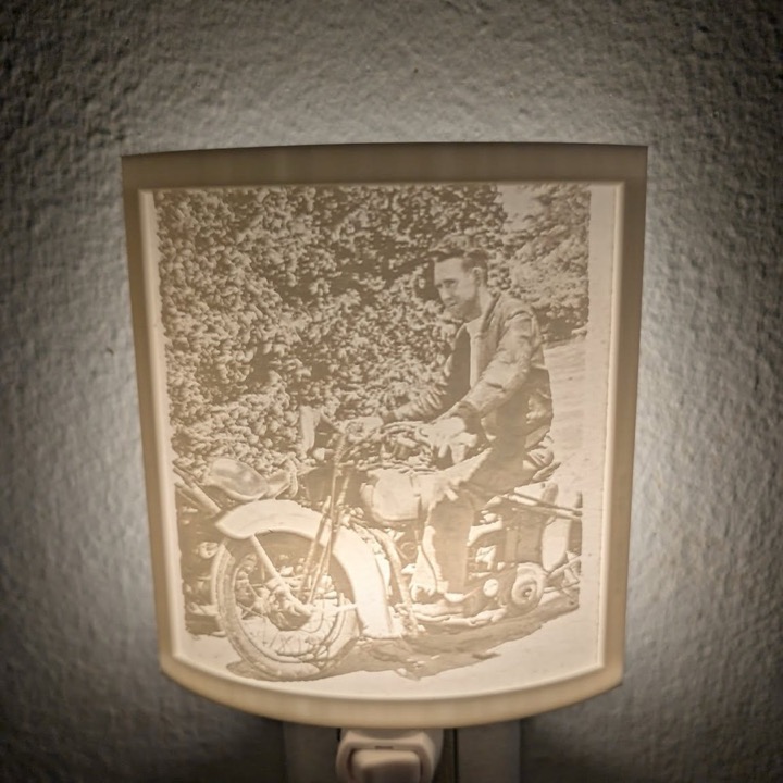 3D printed curved lithophane night light showing a vintage photo of a man on a motorcycle, plugged into a wall outlet